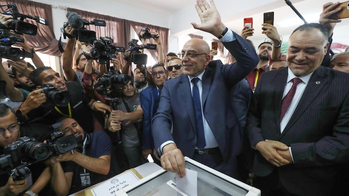 Un homme dépose son bulletin de vote dans l'urne devant une nuée de journalistes.